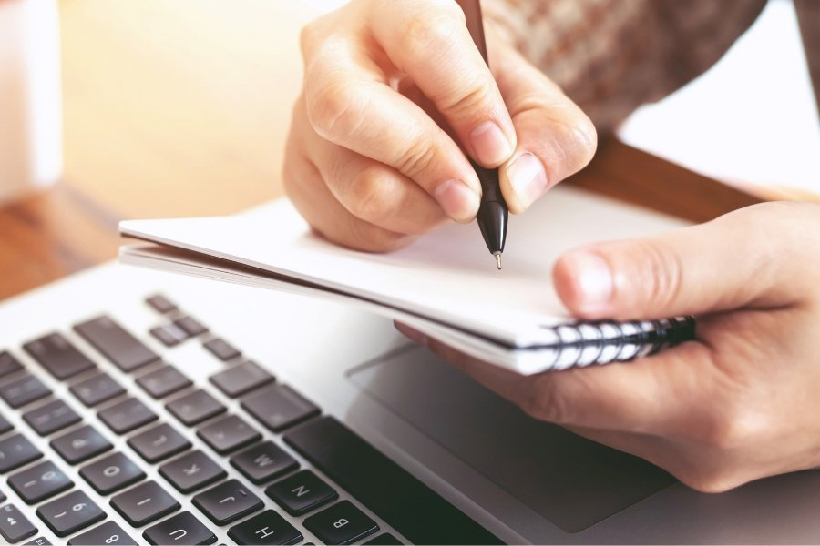 man writing notes in front of laptop